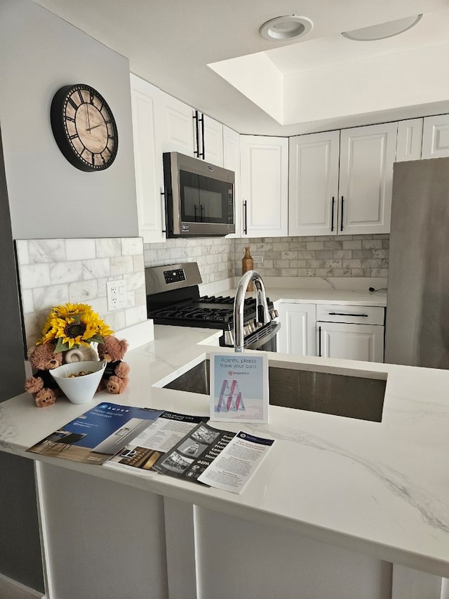 kitchen featuring white cabinets, light stone countertops, stainless steel appliances, and decorative backsplash