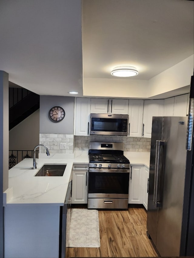 kitchen with light stone counters, light wood-style flooring, stainless steel appliances, a sink, and backsplash