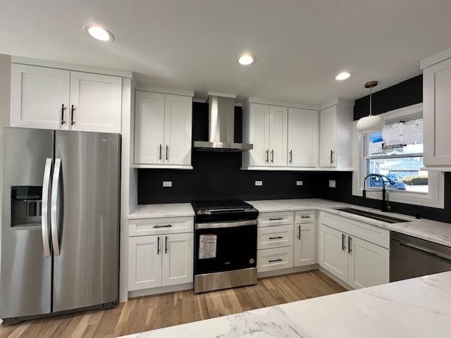 kitchen featuring stainless steel appliances, a sink, white cabinetry, light wood-style floors, and wall chimney range hood