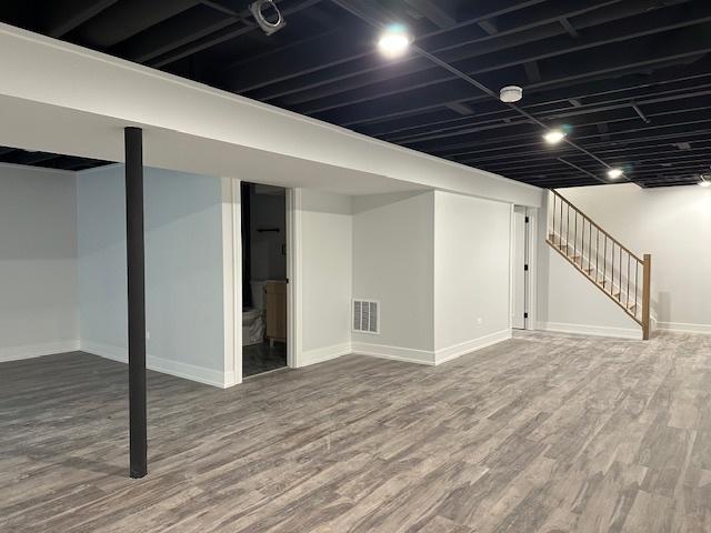 finished below grade area with visible vents, stairway, baseboards, and wood finished floors