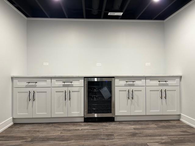 bar with wine cooler, dark wood finished floors, a dry bar, and baseboards