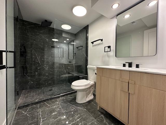 full bathroom featuring toilet, marble finish floor, a marble finish shower, and vanity