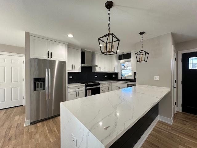 kitchen featuring stainless steel fridge, white cabinets, a peninsula, wall chimney range hood, and black range with electric cooktop