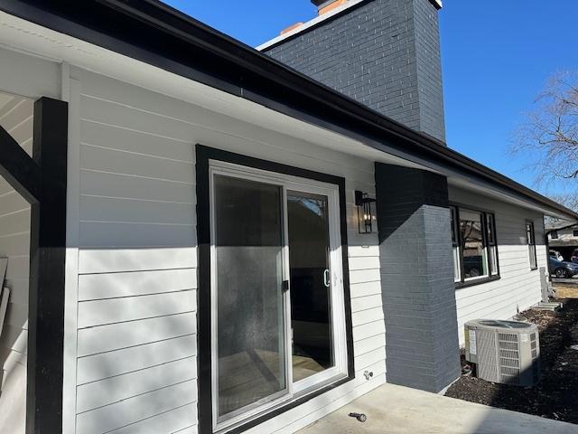 view of exterior entry featuring brick siding, a chimney, and central air condition unit