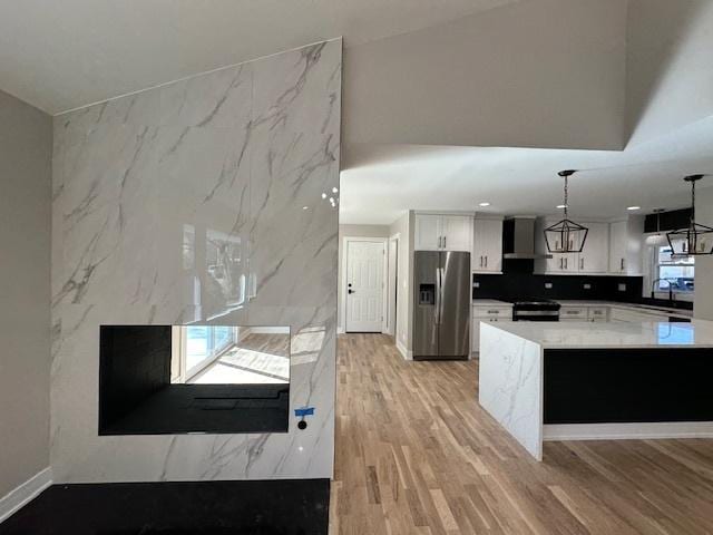 kitchen featuring electric stove, light wood-style floors, white cabinetry, stainless steel fridge, and wall chimney exhaust hood