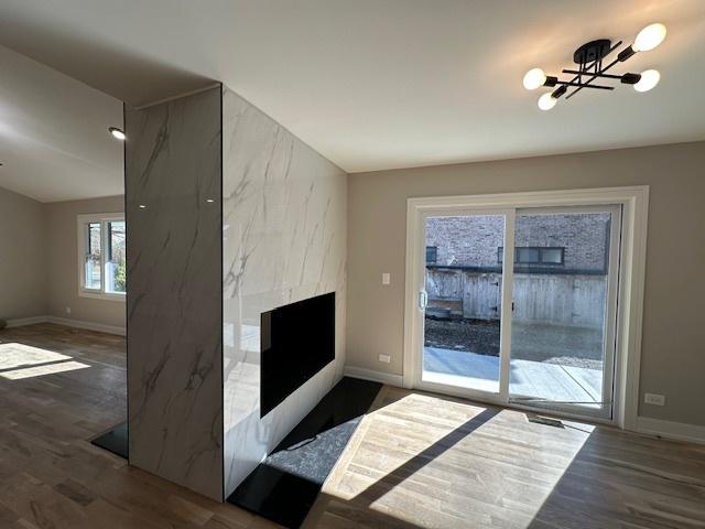 unfurnished living room featuring a fireplace, baseboards, a chandelier, and wood finished floors