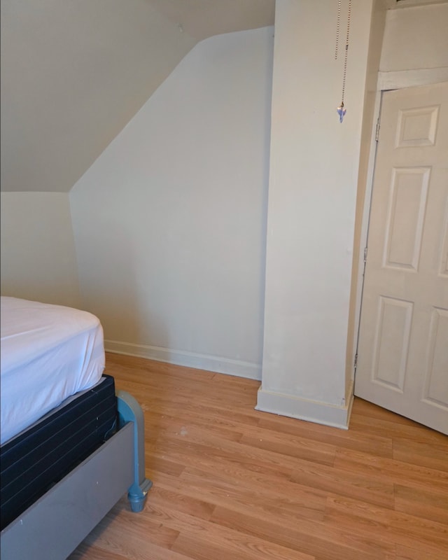 bedroom featuring baseboards, vaulted ceiling, and light wood finished floors