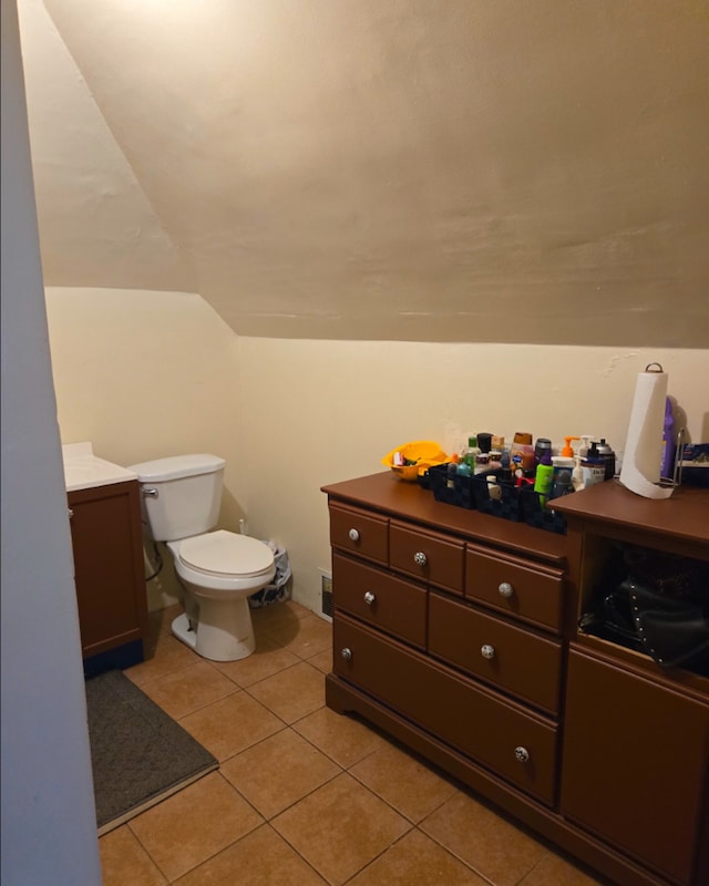 half bathroom with lofted ceiling, vanity, toilet, and tile patterned floors