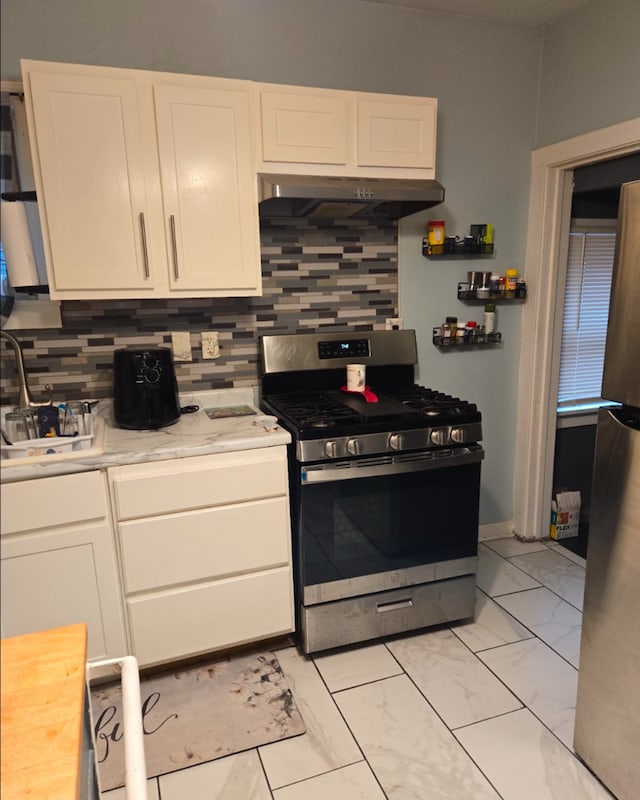 kitchen with stainless steel range with gas cooktop, marble finish floor, backsplash, white cabinetry, and under cabinet range hood