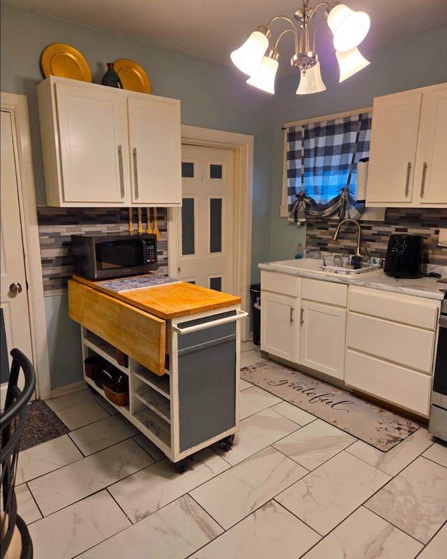 kitchen featuring marble finish floor, backsplash, an inviting chandelier, white cabinetry, and a sink