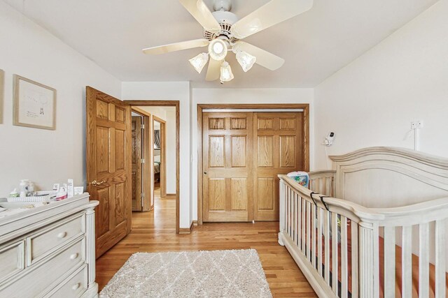 bedroom featuring a closet, ceiling fan, light wood-type flooring, a crib, and baseboards