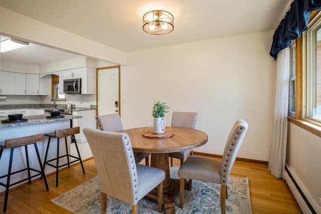 dining space with light wood finished floors, baseboards, and a baseboard heating unit