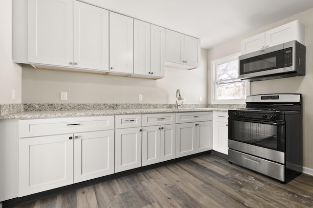 kitchen featuring white cabinets, light stone counters, appliances with stainless steel finishes, dark wood-type flooring, and a sink