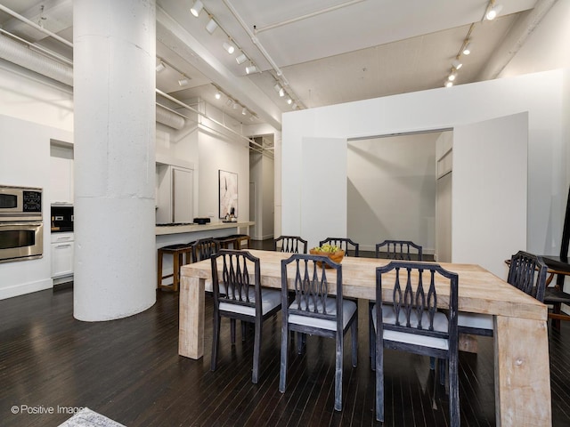 dining room featuring rail lighting, ornate columns, and wood finished floors