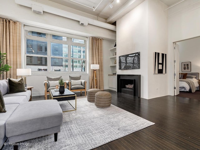 living area with rail lighting, a fireplace, a high ceiling, and wood finished floors