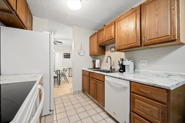 kitchen featuring brown cabinetry, light tile patterned flooring, a sink, dishwasher, and range