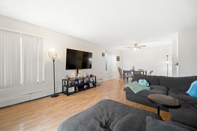 living area with a ceiling fan, wood finished floors, baseboard heating, and a textured ceiling