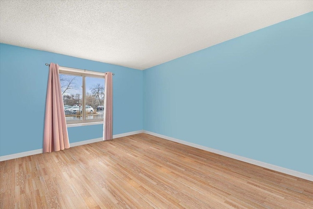 spare room featuring baseboards, light wood-style floors, and a textured ceiling