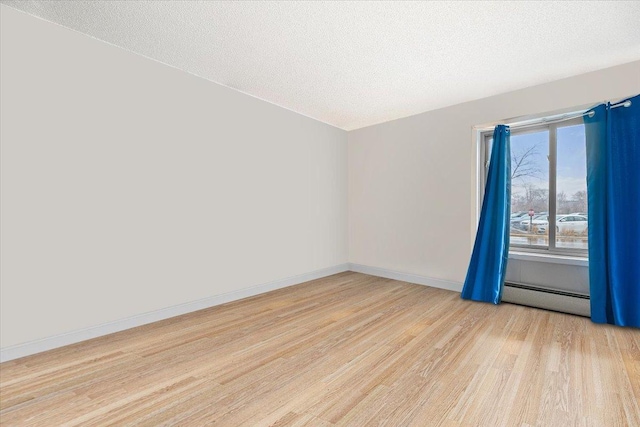 unfurnished room featuring a baseboard heating unit, baseboards, light wood finished floors, and a textured ceiling