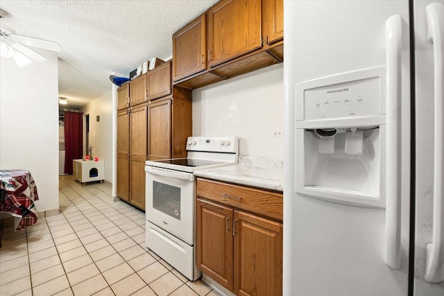 kitchen with light countertops, light tile patterned floors, brown cabinets, white appliances, and a textured ceiling