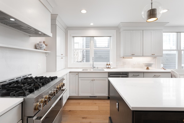 kitchen featuring a sink, light countertops, high end stainless steel range, light wood-type flooring, and decorative light fixtures