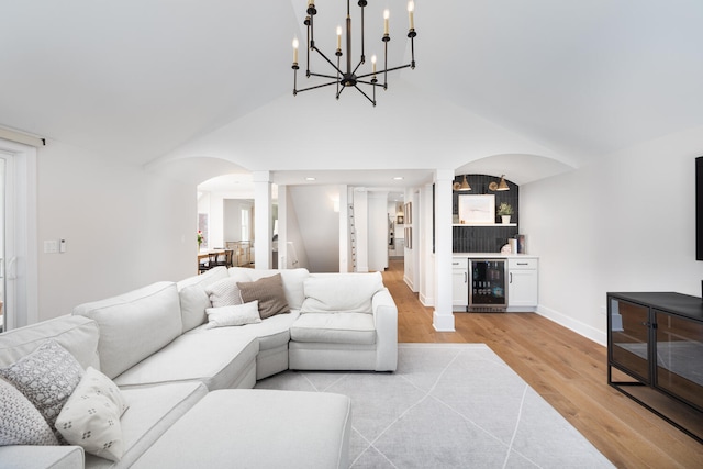 living room featuring arched walkways, beverage cooler, light wood finished floors, and ornate columns