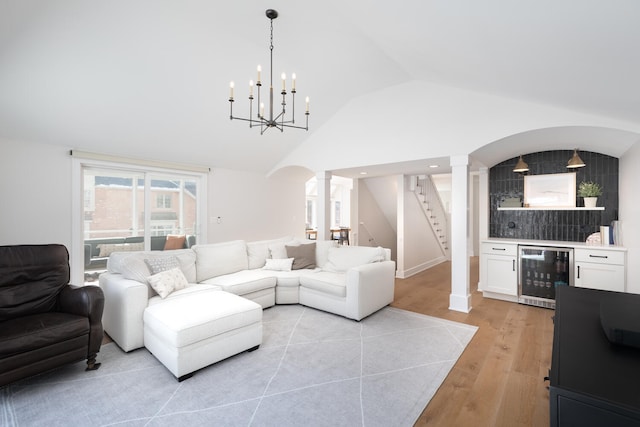 living area featuring beverage cooler, a bar, stairway, light wood-type flooring, and ornate columns