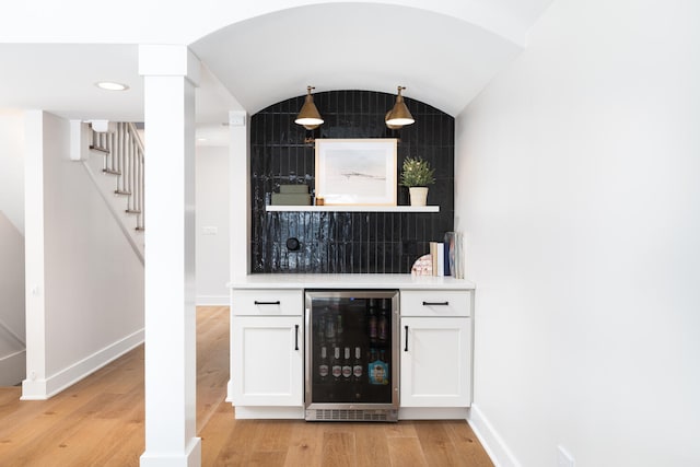 bar with a bar, beverage cooler, light wood-style flooring, and baseboards