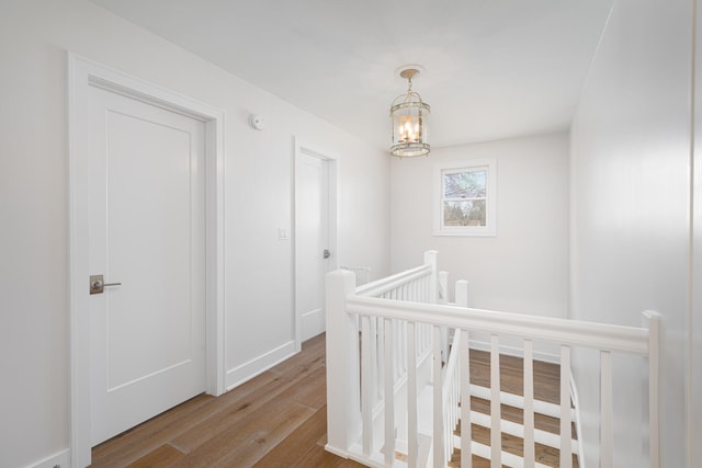 hall featuring an inviting chandelier, baseboards, wood finished floors, and an upstairs landing