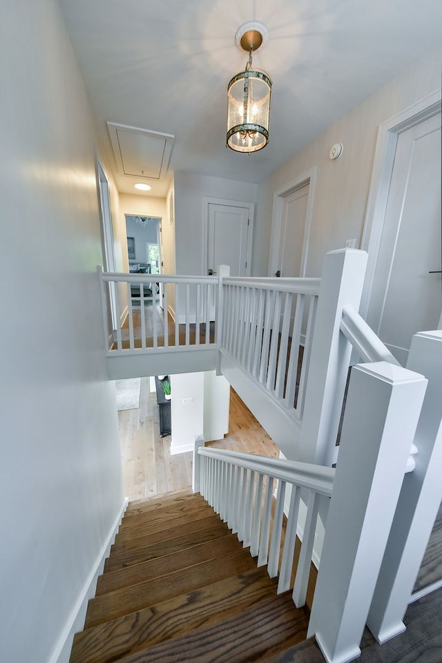 stairs featuring baseboards, attic access, a chandelier, and wood finished floors