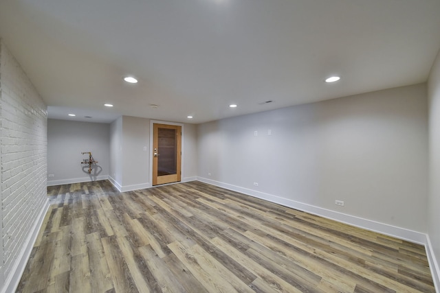 spare room with brick wall, baseboards, wood finished floors, and recessed lighting