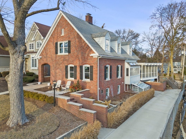 view of front of home featuring a patio area, brick siding, a chimney, and roof with shingles