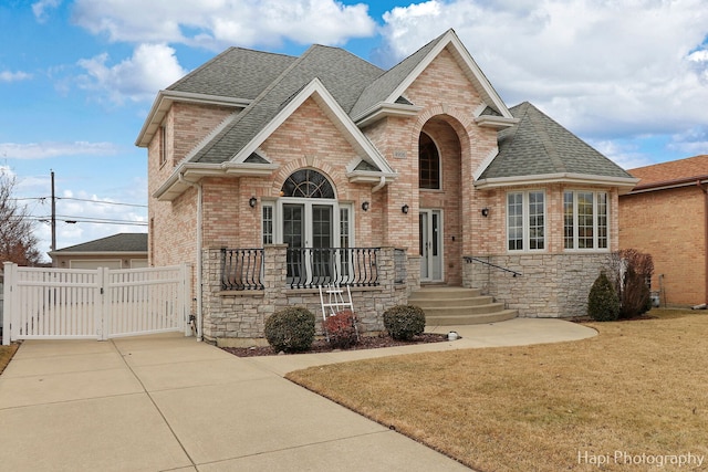 view of front facade featuring brick siding, driveway, stone siding, roof with shingles, and a gate