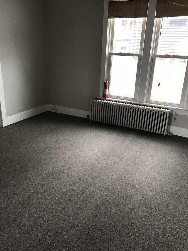 spare room with baseboards, radiator heating unit, and carpet flooring
