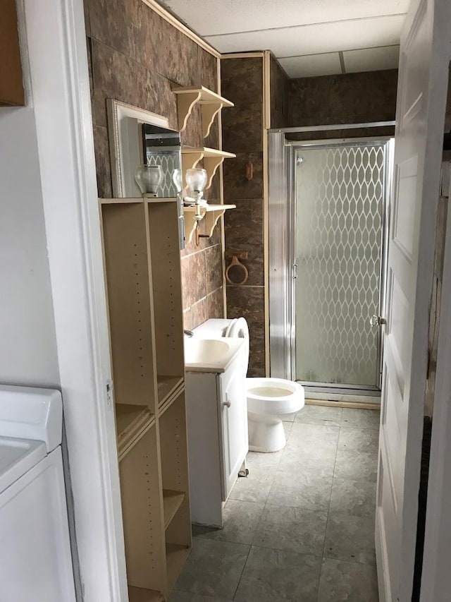 full bathroom with tile walls, a shower stall, toilet, vanity, and washing machine and dryer