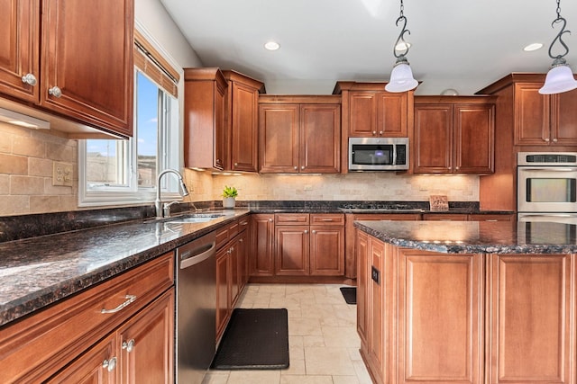 kitchen with a sink, hanging light fixtures, appliances with stainless steel finishes, backsplash, and dark stone countertops
