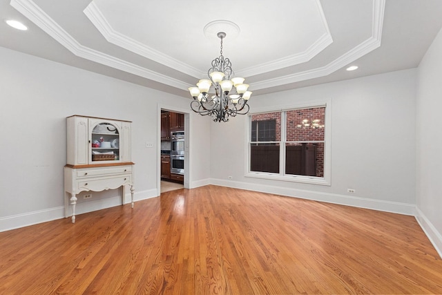 unfurnished room featuring a tray ceiling, an inviting chandelier, light wood-style floors, ornamental molding, and baseboards