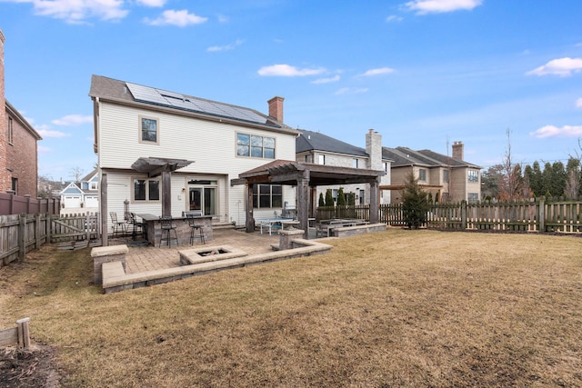 rear view of house with a fire pit, a lawn, solar panels, a patio, and a fenced backyard