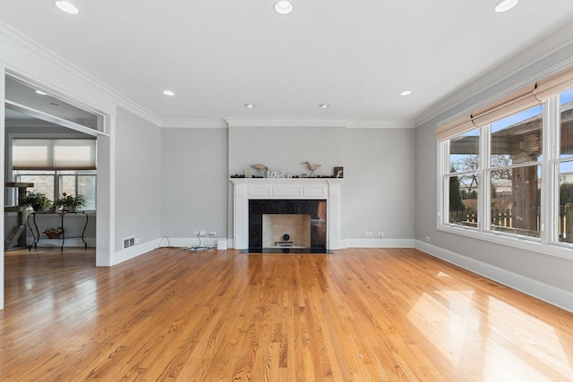unfurnished living room featuring ornamental molding, a tiled fireplace, light wood-style flooring, and baseboards