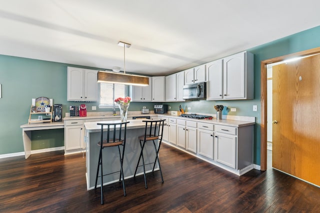 kitchen featuring gas cooktop, a breakfast bar, light countertops, dark wood-style floors, and stainless steel microwave