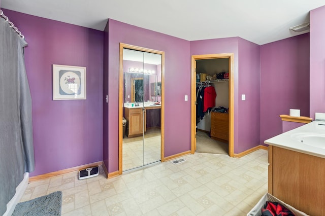 bathroom featuring baseboards, visible vents, a walk in closet, and vanity