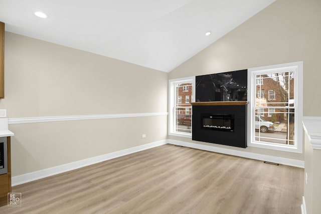 unfurnished living room featuring lofted ceiling, a fireplace, wood finished floors, and a wealth of natural light