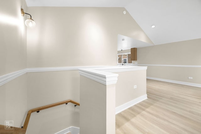 hallway featuring baseboards, vaulted ceiling, an upstairs landing, and wood finished floors