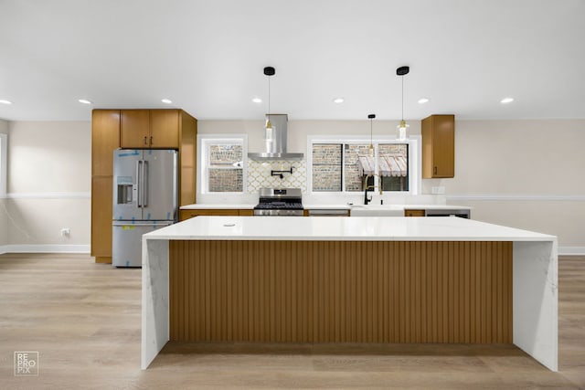 kitchen with stainless steel appliances, tasteful backsplash, a sink, wall chimney range hood, and light wood-type flooring