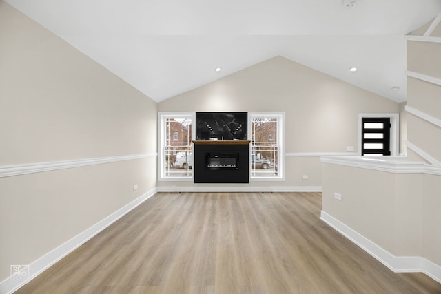 unfurnished living room featuring a glass covered fireplace, lofted ceiling, baseboards, and wood finished floors