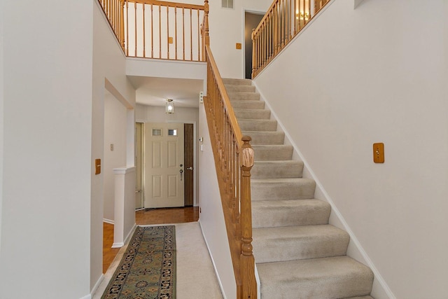 stairway featuring visible vents, baseboards, and a high ceiling