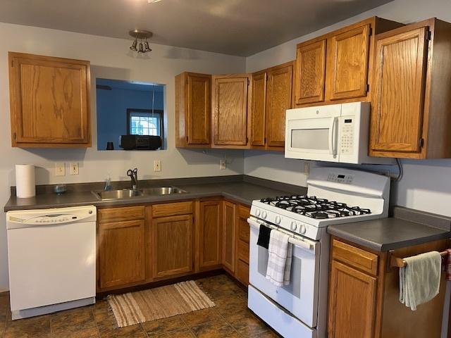 kitchen featuring dark countertops, white appliances, brown cabinetry, and a sink