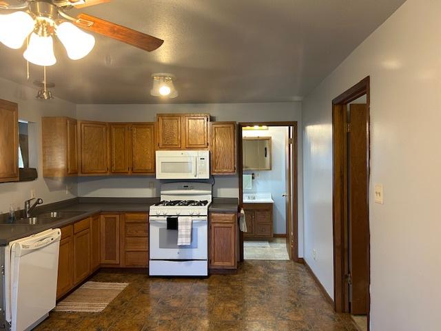 kitchen featuring white appliances, brown cabinetry, and dark countertops