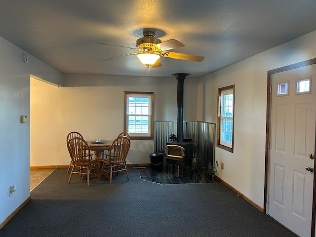 carpeted dining area featuring a wood stove, ceiling fan, and baseboards