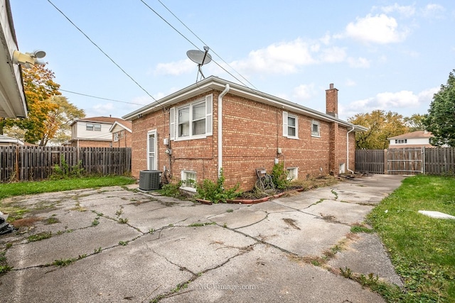 view of property exterior featuring central AC unit, a chimney, fence, a patio area, and brick siding